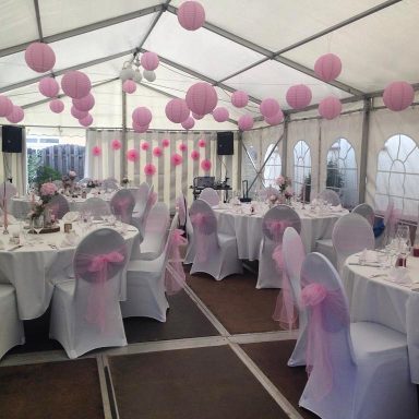 Runde Tische und Stühle in Weiß, mit rosa Ballons im Zelt